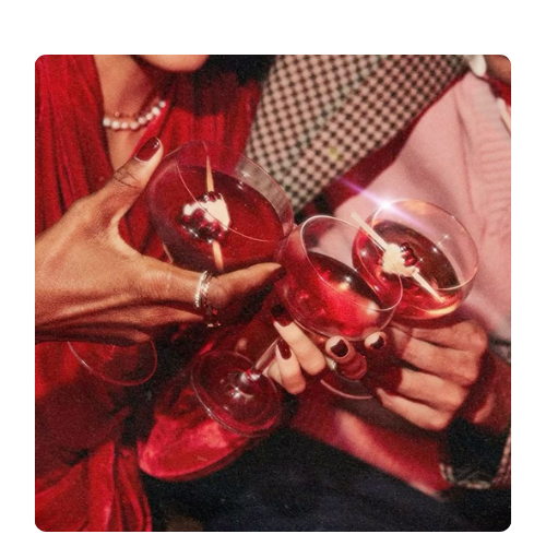 Verres à cocktail rouges portés pour un toast Trois personnes trinquent avec des coupes de cocktail rouges, dans une ambiance festive et élégante, évoquant la convivialité et les moments partagés.